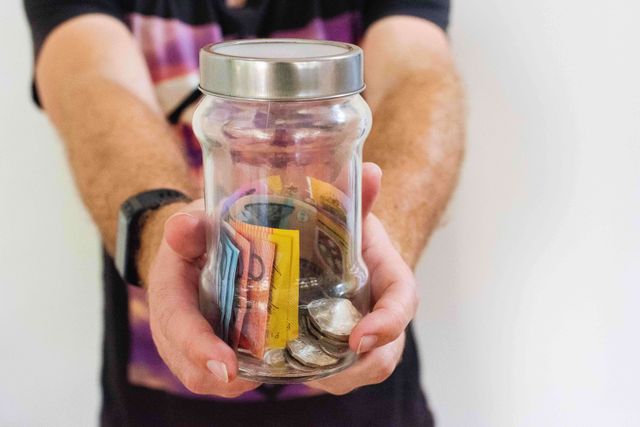 A man holding a jar of Australian money.