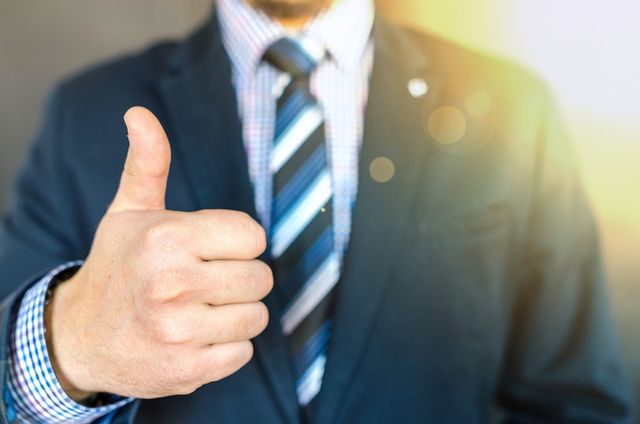 Close up photo of man wearing black suit jacket doing thumbs up