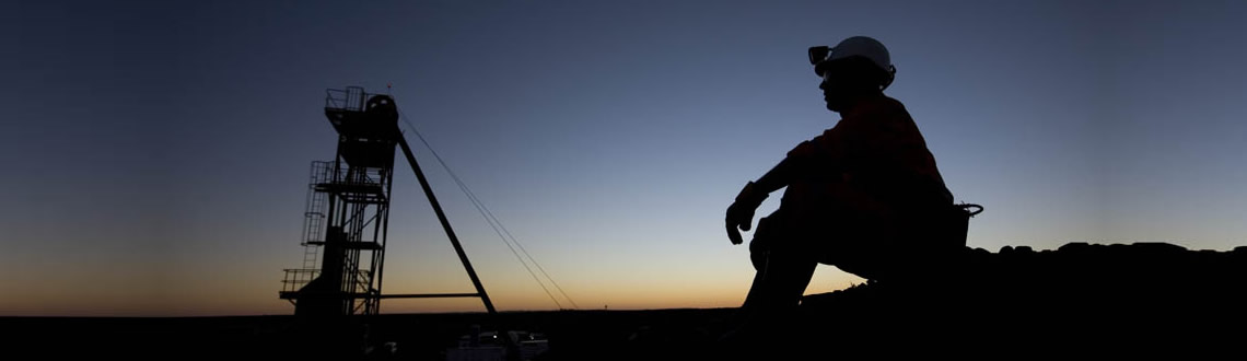Silhouette of miner with helmet and processing plant against sunrise sky